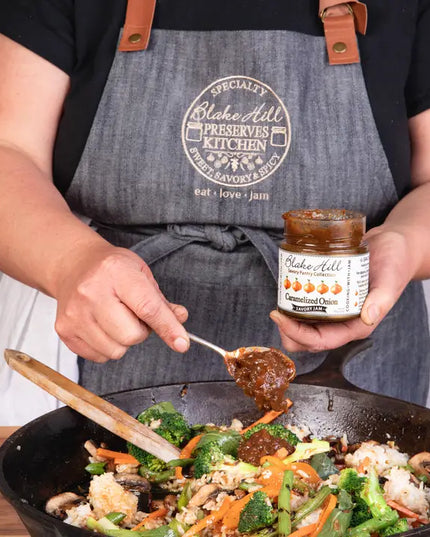 Person cooking with a jar of Blake Hill Preserves in a kitchen setting
