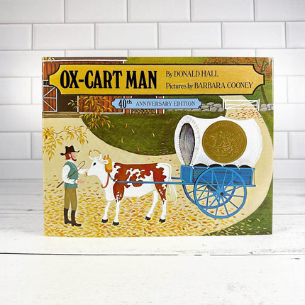 Book cover of 'Ox-Cart Man' with a farmer and oxen illustration on a white brick background
