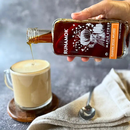 Person pouring Runamok maple syrup into a cup of coffee with a blurred background
