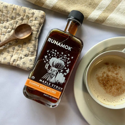 Bottle of Runamok maple syrup next to a cup of coffee on a white surface.