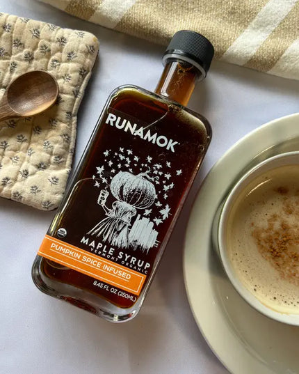 Bottle of Runamok maple syrup next to a cup of coffee on a white surface.