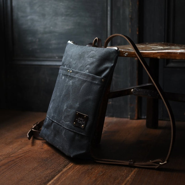the Day Pack in Ash rests against a chair in a dark rustic room