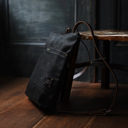 the Day Pack in Chocolate rests against a chair in a dark rustic room