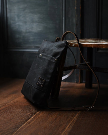 the Day Pack in Chocolate rests against a chair in a dark rustic room
