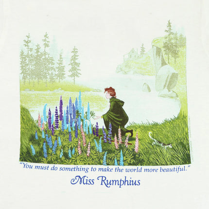 closeup of the tee shirt graphic showing Miss Rumphuis kneeling down to admire Lupine flowers against a coastal Maine landscape