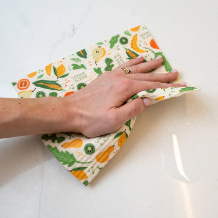 Hand using a reusable cloth with fruit pattern to clean a white surface