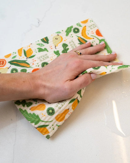 Hand using a reusable cloth with fruit pattern to clean a white surface