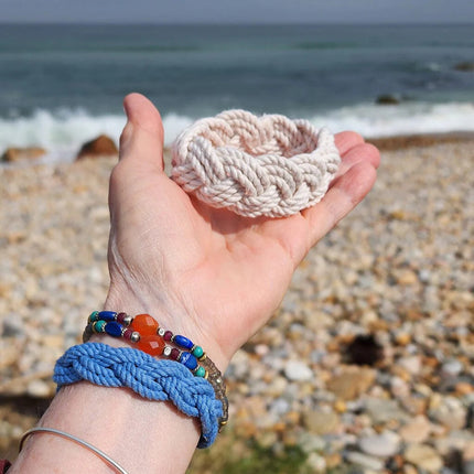 an outstretched hand holding a sailor bracelet with sandy shores and the ocean in the background