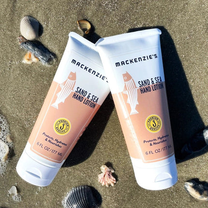 Two bottles of the Sand and Sea Hand Lotion on a sandy beach