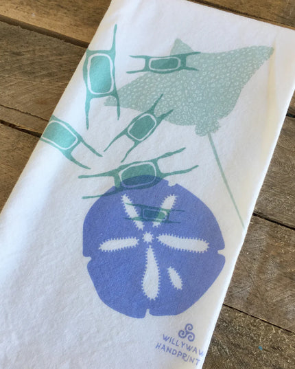 White towel with blue sand dollar and green sea urchin design on a wooden surface