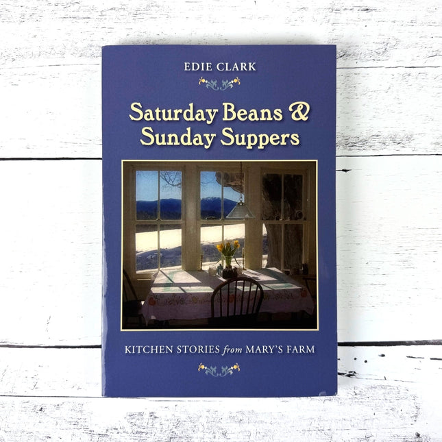 book titled Saturday Beans and Sunday Suppers by Edie Clark - blue cover with painting of a kitchen table near a window with a sunny winter landscape