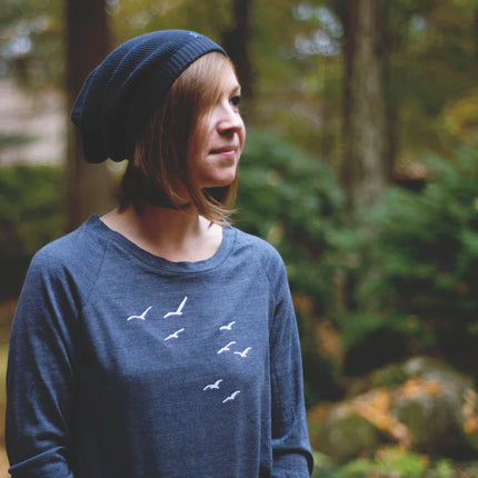 Person wearing a blue beanie and shirt with bird design in a forest setting