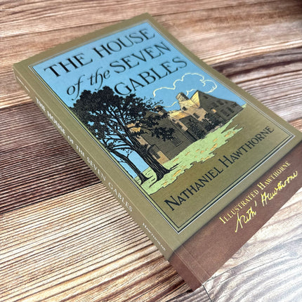 House of the Seven Gables book laid on a rustic wood surface, shown at a slight side angle revealing the title text along the spine of the book