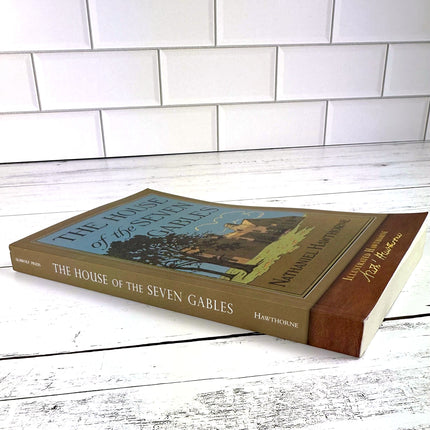 House of the Seven Gables book laid flat on a white wood surface and shown from a slight side angle, so the spine of the book is visible
