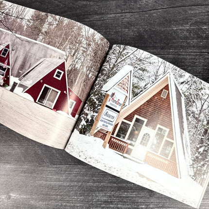 Open book showing two A-frame houses with snow-covered roofs on a wooden surface.