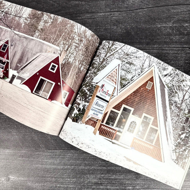 Open book showing two A-frame houses with snow-covered roofs on a wooden surface.