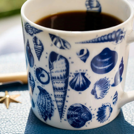 White mug with blue shell pattern filled with coffee on a textured surface