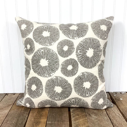 Decorative pillow with gray circular pattern on a wooden surface and white wooden panel background