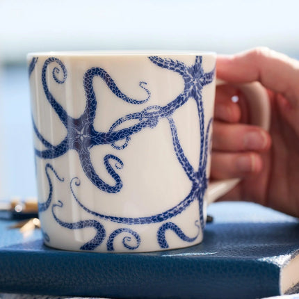 Mug with blue starfish design held by a hand on a blue surface