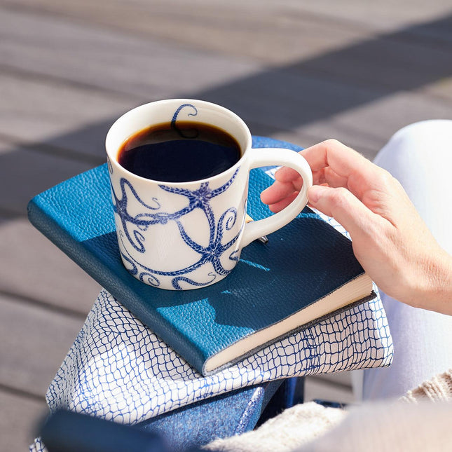 Person holding a cup of coffee on a blue textured surface outdoors