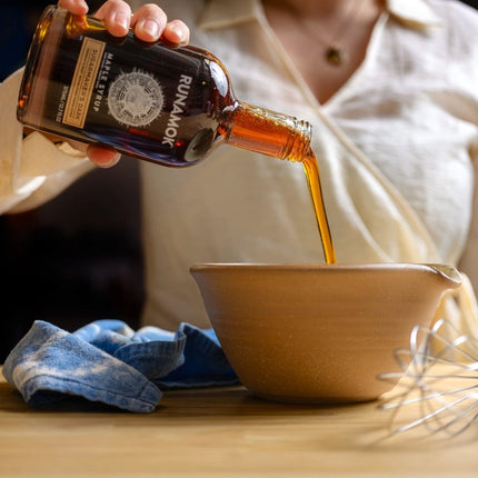 a countertop with a mixing bowl and whisk and a hand pouring syrup into the mixing bowl