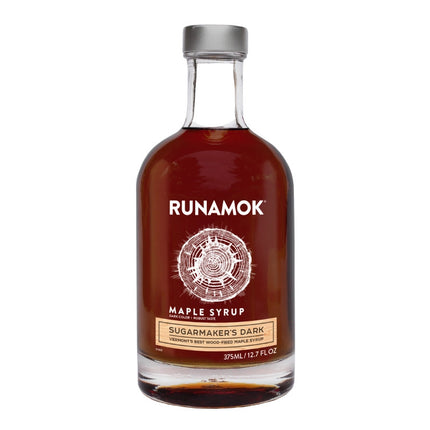 a clear glass bottle filled with dark amber colored maple syrup with an elegant label that reads "Runamok Maple Syrup Sugarmaker's Dark" with a graphic of a cross section of a maple tree