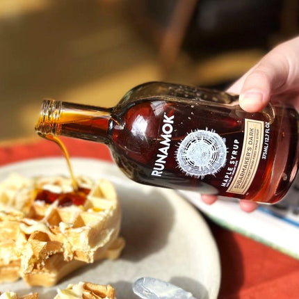 a close up of a bottle of Sugarmaker's Dark maple syrup being poured onto a stack of waffles