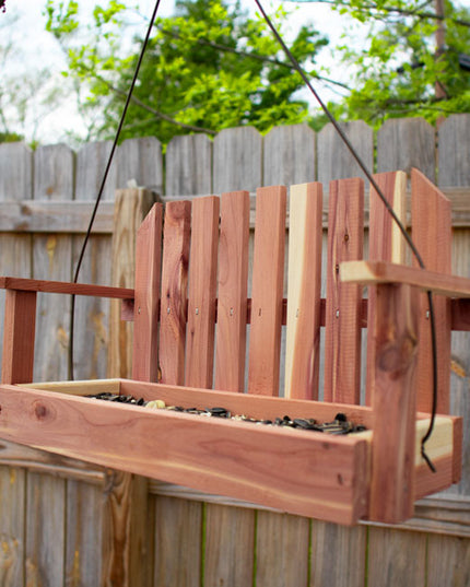 the cedar swing bird feeder hanging from a tree in a backyard with a wooden fence in the background