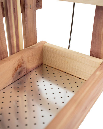 a close up view of the seat of the cedar swing bird feeder showing the empty seat of the swing with metal perforated base to keep seed aerated