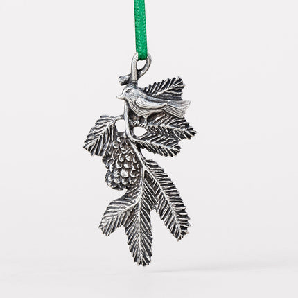 A delicately detailed handcrafted pewter ornament of a bird on a pine bough with a green silk ribbon