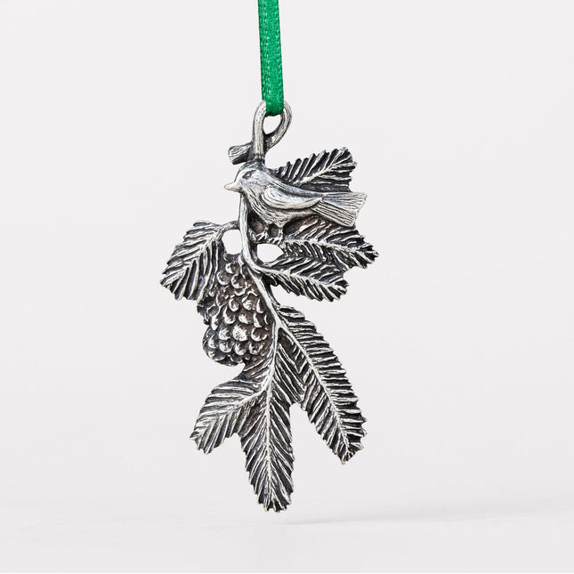 A delicately detailed handcrafted pewter ornament of a bird on a pine bough with a green silk ribbon