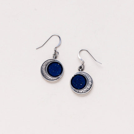 Handcrafted silver Crescent Moon Earrings featuring a stippled surface resembling moon craters, with a sparkling blue inner section, showcasing celestial beauty