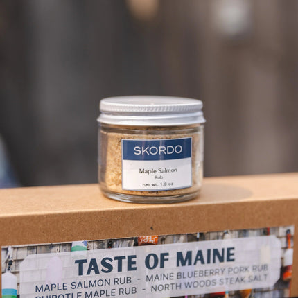 Jar of Skordo Maple Salmon Rub on a wooden surface with 'Taste of Maine' branding in the background.