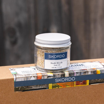 Skordo North Woods Steak Salt jar on a wooden surface with a blurred background