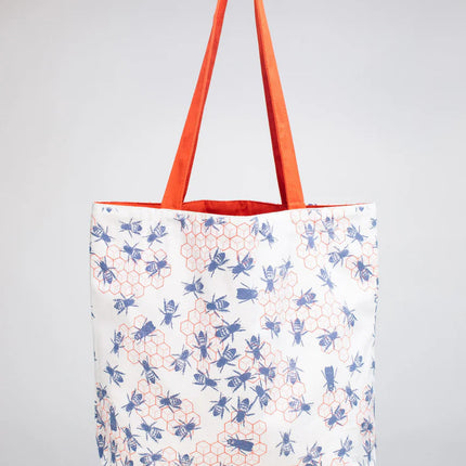 side one of the bee hive tote - a white tote bag with orange straps with a repeated orange honeycomb design that is adorned with blue bees