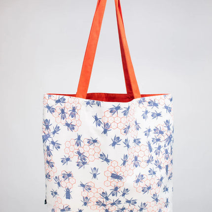 side two of the bee hive tote - a white tote bag with orange straps with a repeated orange honeycomb design that is adorned with blue bees