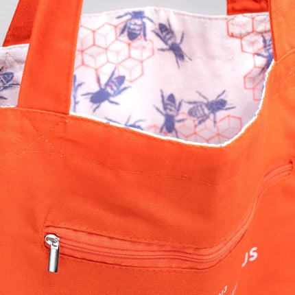 a close up of the tote near the handles showing the bag reversed so the bee hive print is on the inside of the tote and the outside is now a vibrant orange