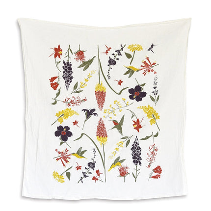 A white tea towel with botanical illustrations of flowers that hummingbirds enjoy with some ruby throated hummingbirds flitting from flower to flower