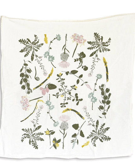 an off white tea towel with colorful botanical illustrations of edible wild foods including clover, herbs, asparagus, and more