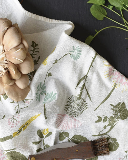 close up of the edible wilds tea towel in use holding foraged mushrooms, a foraging knife, and herbs