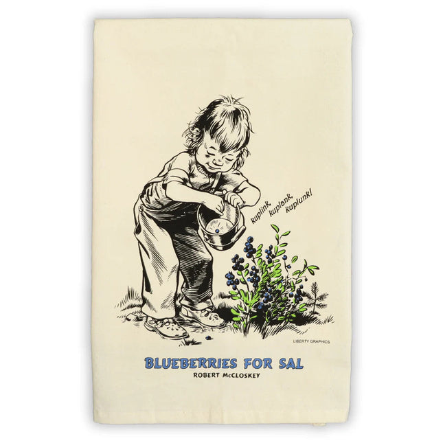 a folded tea towel featuring artwork from Blueberries for Sal of Sal picking blueberries and dropping them into her bucket