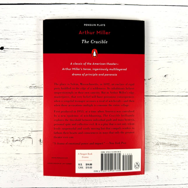 Back cover of 'The Crucible' by Arthur Miller with red and black design on a white wooden surface.