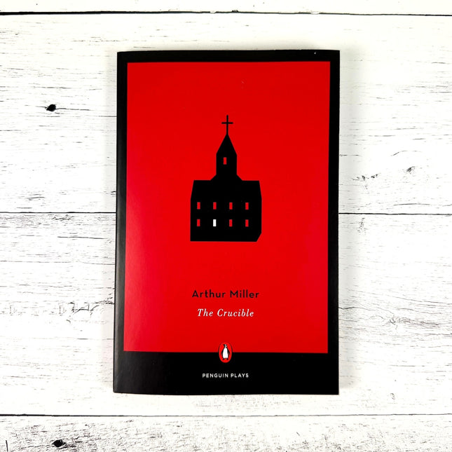 paperback copy of 'The Crucible' by Arthur Miller with red book cover and silhouette of a church on a white wood surface