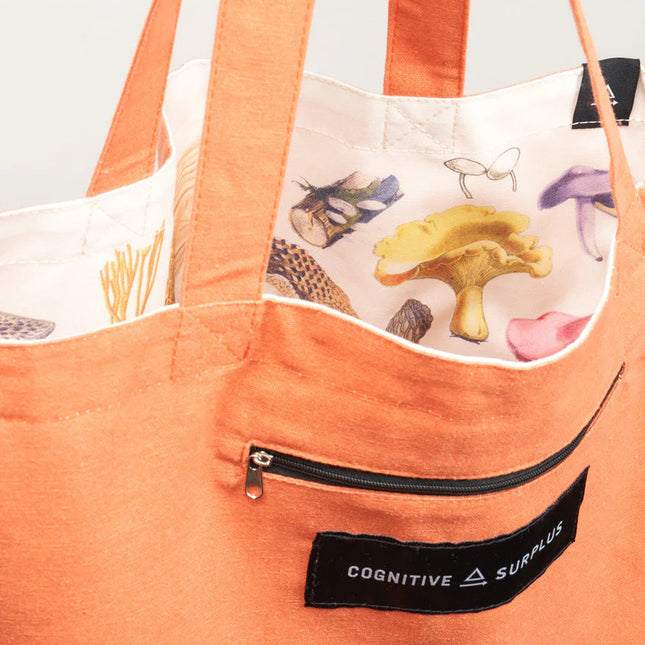 a close up of the tote near the handles showing the bag reversed so the mushroom print is on the inside of the tote and the outside is now a tangerine orange