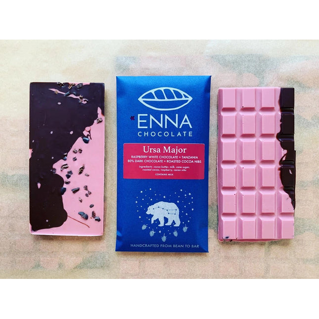 Three Ursa Major bars side by side. The center bar is in its royal blue wrapper with ursa major constellation illustration and the two surrounding bars are unwrapped and showing off their brilliant pink color swirled with dark chocolate and speckled with cacao nibs