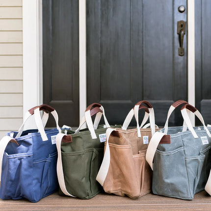 Four tote bags in blue, green, brown, and gray in front of a door.