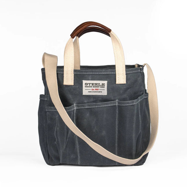 Dark gray waxed canvas tote bag with beige straps and leather handle on a white background