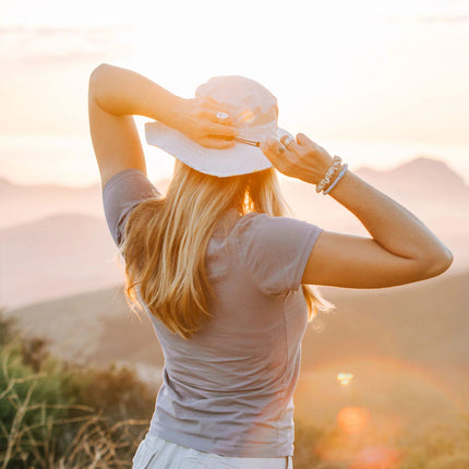 a model wearing the Venture sun hat with their back to the viewer and hands at the back of their head about to pull their hair through the ponytail hole in the back of the hat
