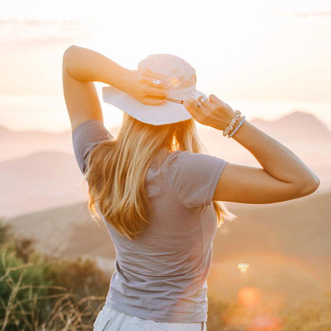 a model wearing the Venture sun hat with their back to the viewer and hands at the back of their head about to pull their hair through the ponytail hole in the back of the hat