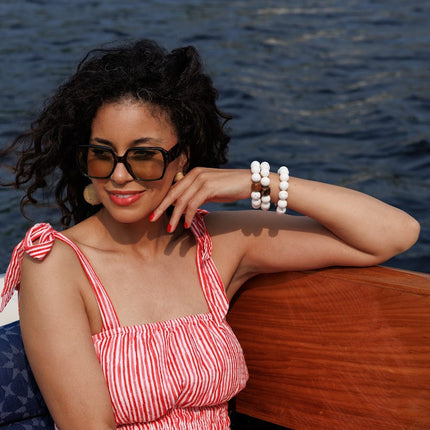 Woman in a red and white striped dress with multiple white beaded bracelets on her wrist sitting on a boat with water in the background